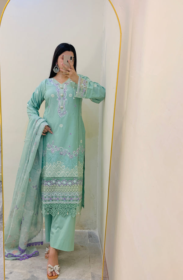 Person wearing a light green traditional outfit with embroidery in front of a mirror.